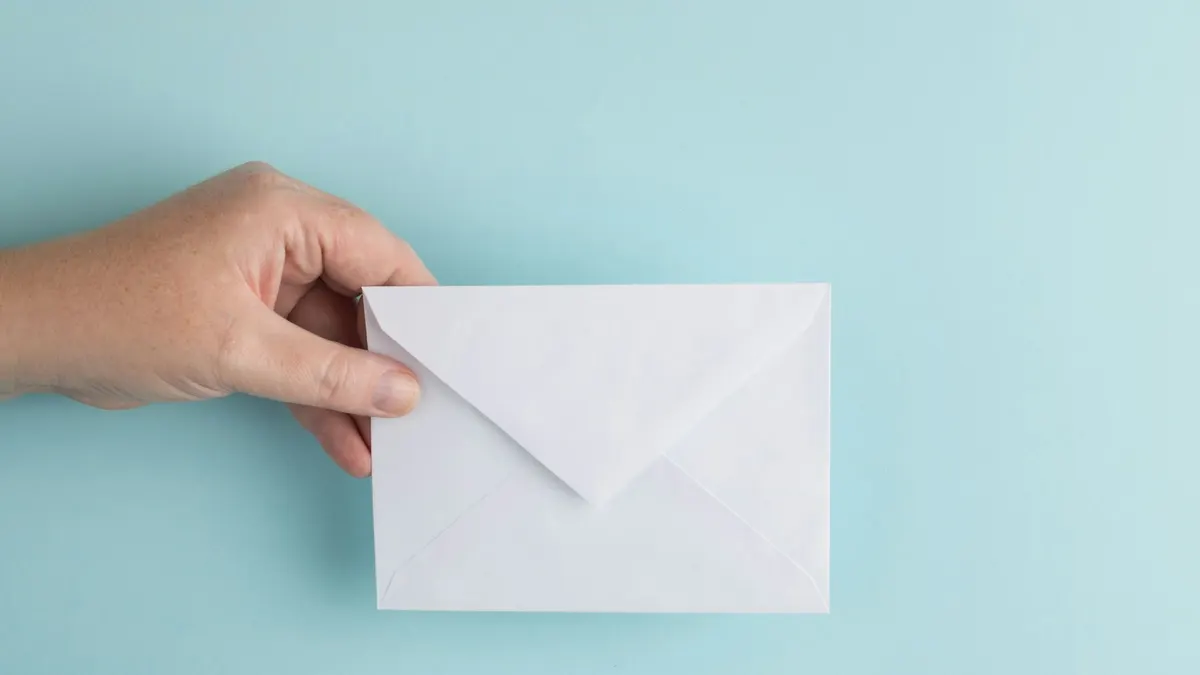A hand holding a sealed white envelope against a light blue background, representing a timeshare cancellation letter ready to be sent by certified mail