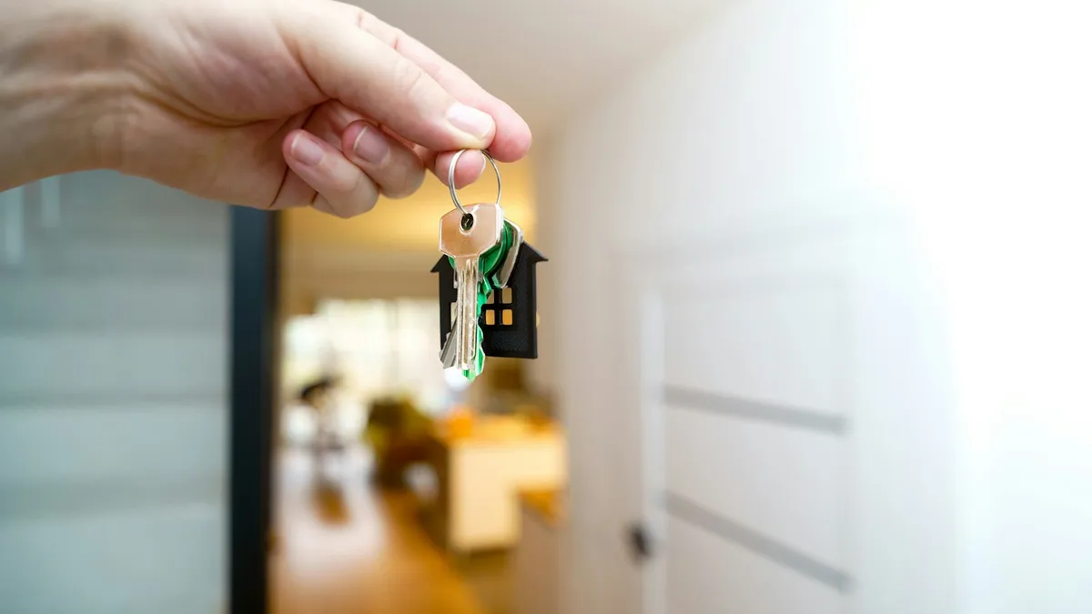 A hand holding a set of house keys on a house-shaped key ring, representing a U.S. timeshare owner handing their ownership back to the resort