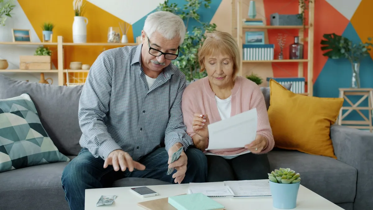 An older couple on a sofa reviewing documents and bills together, representing U.S. timeshare owners gathering the paperwork needed for a timeshare surrender
