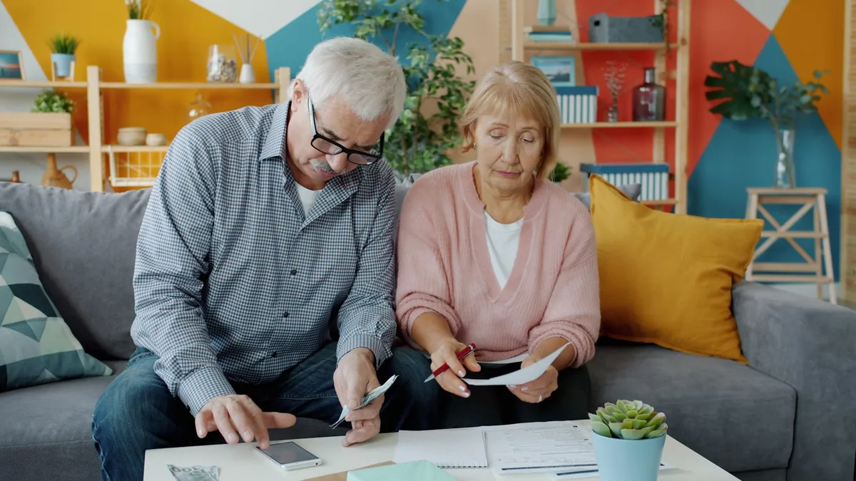 An older couple sitting at home reviewing paperwork and fee statements together, representing U.S. timeshare owners assessing their contract before a sale or exit