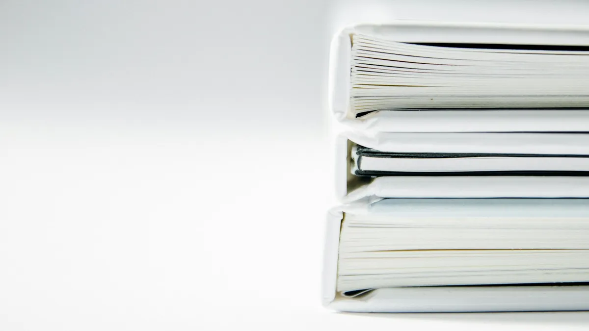 A stack of thick white document binders on a plain background, representing the deed, contract, and fee records a U.S. owner gathers before starting a timeshare exit
