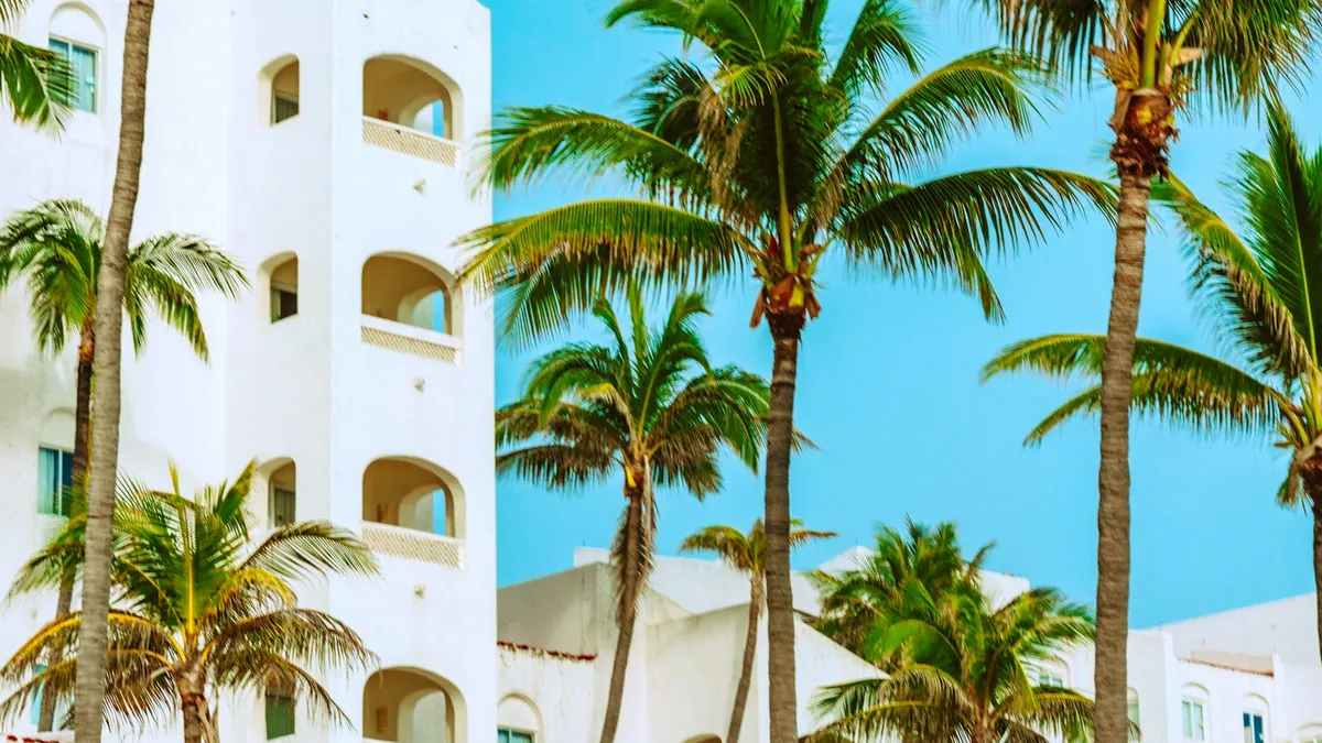 A white resort building framed by palm trees under a bright blue sky, representing the paid-off timeshare a U.S. owner is trying to leave behind