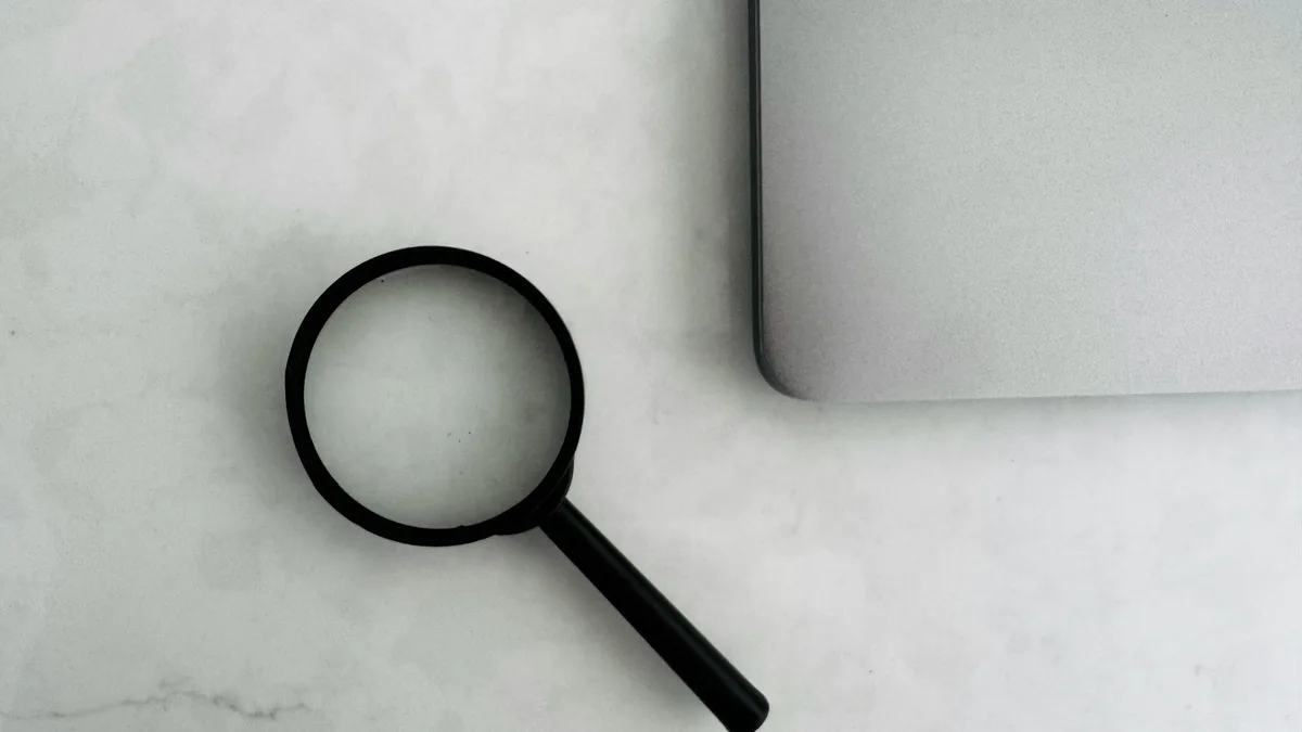 A magnifying glass resting beside a laptop on a desk, representing the verification U.S. owners should perform before hiring a timeshare resale or exit firm