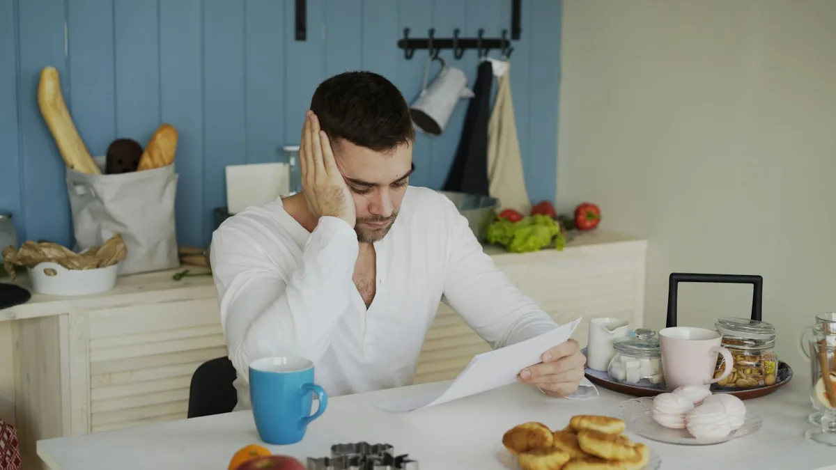 A man sitting at a kitchen table holding his head while reading a billing notice, representing a U.S. owner facing collection activity on an unpaid special assessment