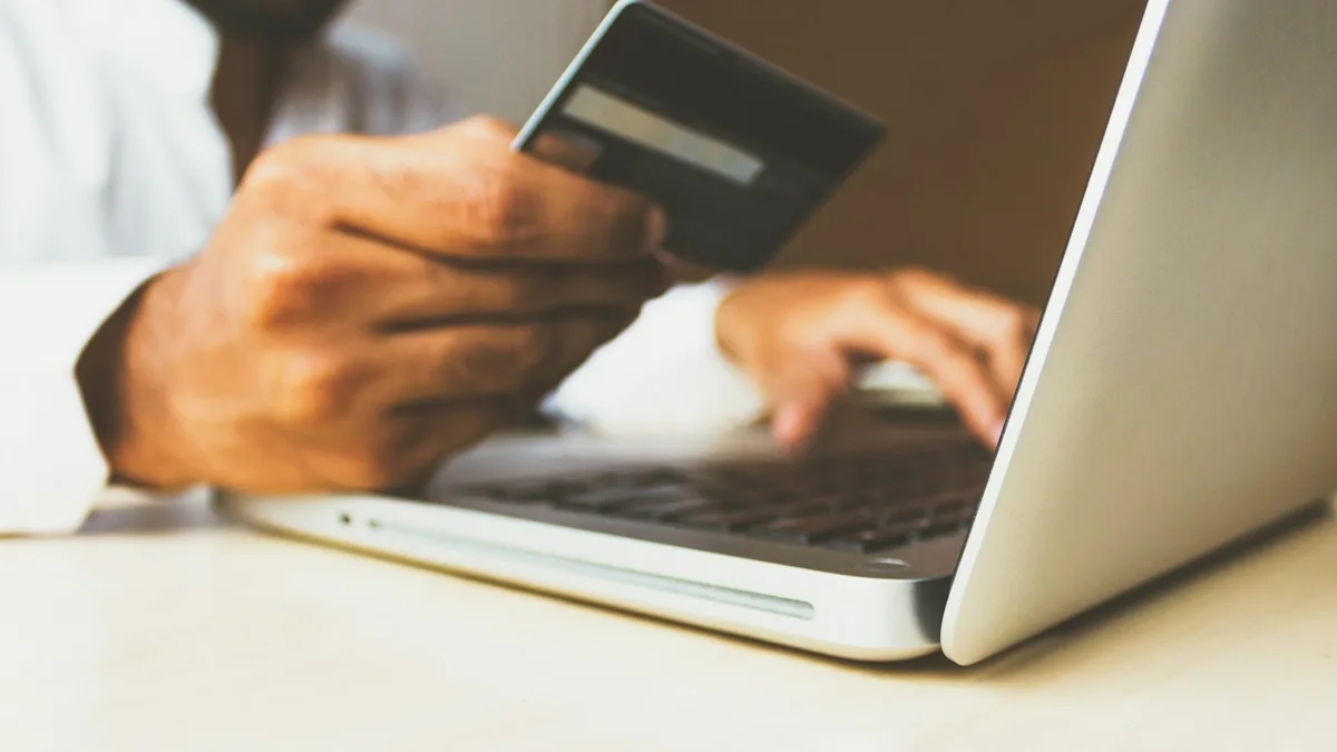 A person holding a credit card while using a laptop, representing the credit score damage caused by missed timeshare payments