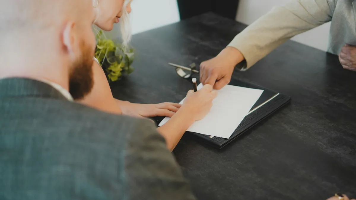 A couple signing a document handed across a desk, representing a U.S. owner getting deed back release terms in writing before agreeing to a timeshare surrender