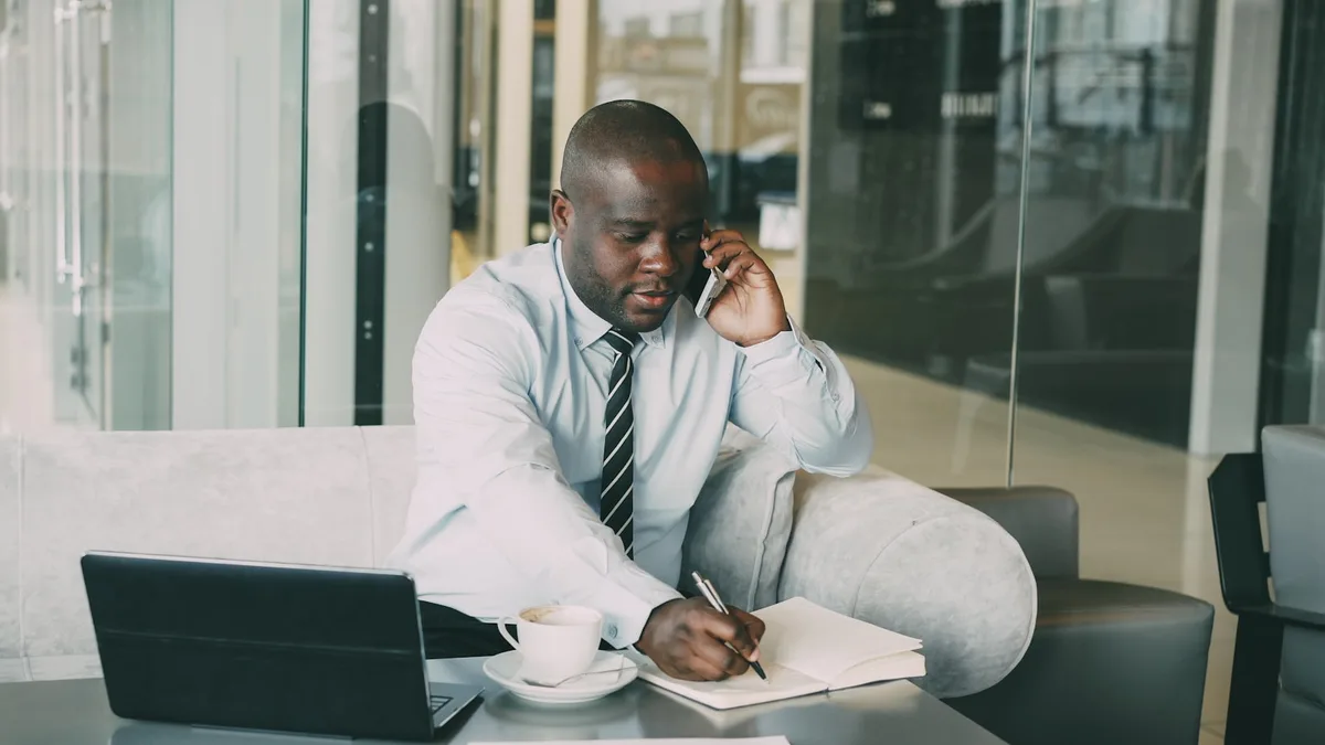 A man at a desk taking written notes during a phone call, representing a U.S. timeshare owner documenting contact from a resort billing department or collector