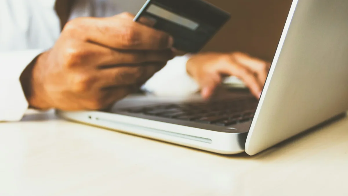 A person holding a credit card at a laptop, representing the per-transaction fee an exchange network collects when a timeshare trade is confirmed