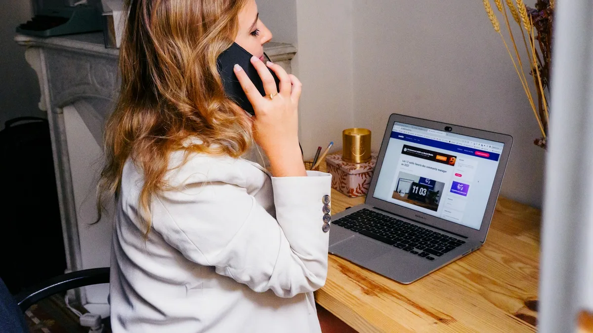 A person taking a phone call at a desk beside a laptop, representing the unsolicited exit offers that signal a timeshare scam