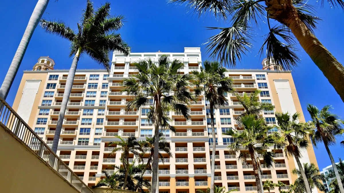 A tall timeshare resort tower framed by palm trees against a clear blue sky, representing the resort ownership that carries rising maintenance fees