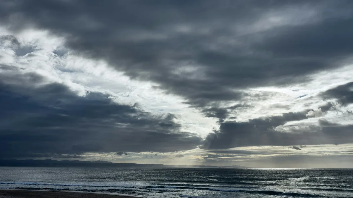 Dark storm clouds gathering over a coastline and beach, representing the hurricane exposure that drives insurance shortfalls and special assessments at U.S. coastal resorts