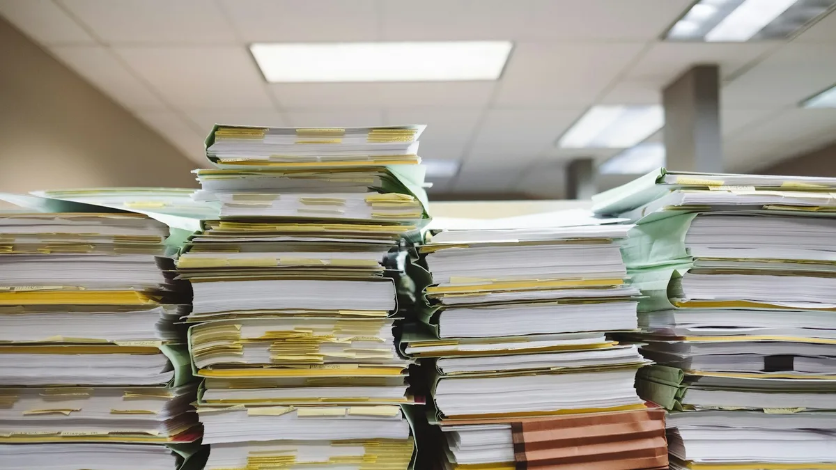 Tall stacks of tabbed file folders and paperwork in an office, representing the complete ownership file a U.S. owner should assemble before choosing an exit path