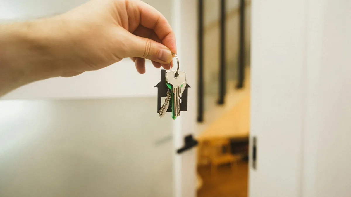 A hand holding a set of house-shaped keys in a doorway, representing the legal handover of timeshare ownership from one U.S. party to another