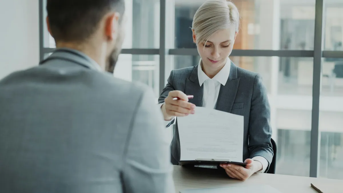 An adviser in a suit handing a contract across an office desk to a seated client, representing an heir reviewing inherited timeshare documents with an attorney