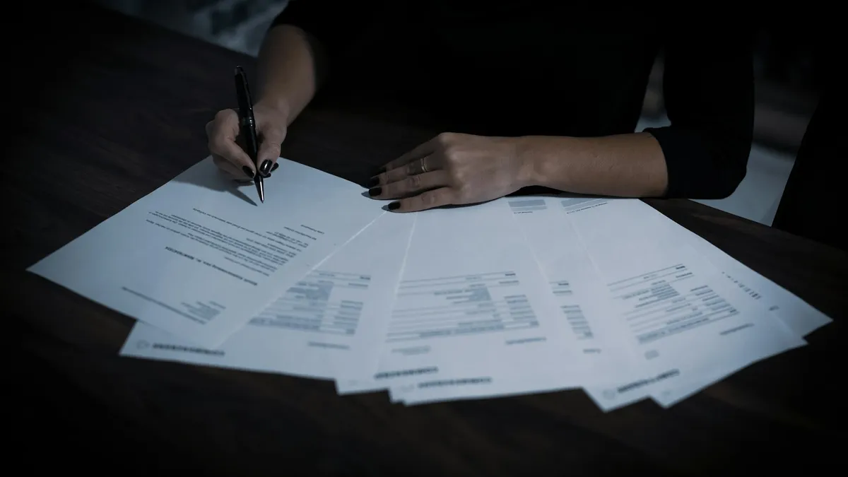 A woman signing printed paperwork spread across a dark wooden table, representing the written disclaimer a U.S. heir files to refuse an inherited timeshare