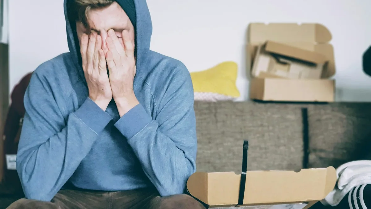 A man in a hooded sweatshirt sitting with his face in his hands, representing the stress U.S. timeshare owners feel from rising costs they cannot control